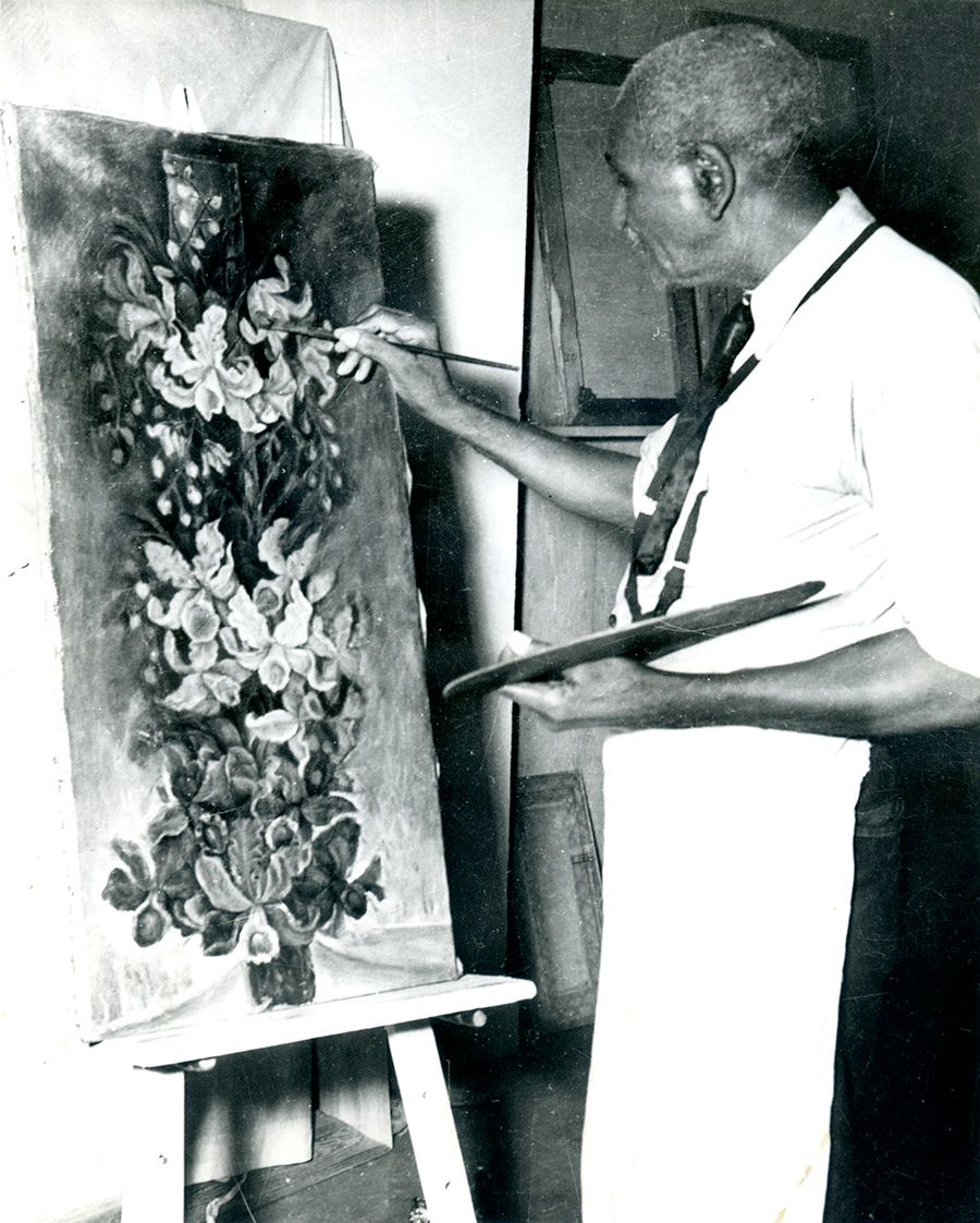 Man painting a floral artwork on an easel, holding a brush and palette in a studio.