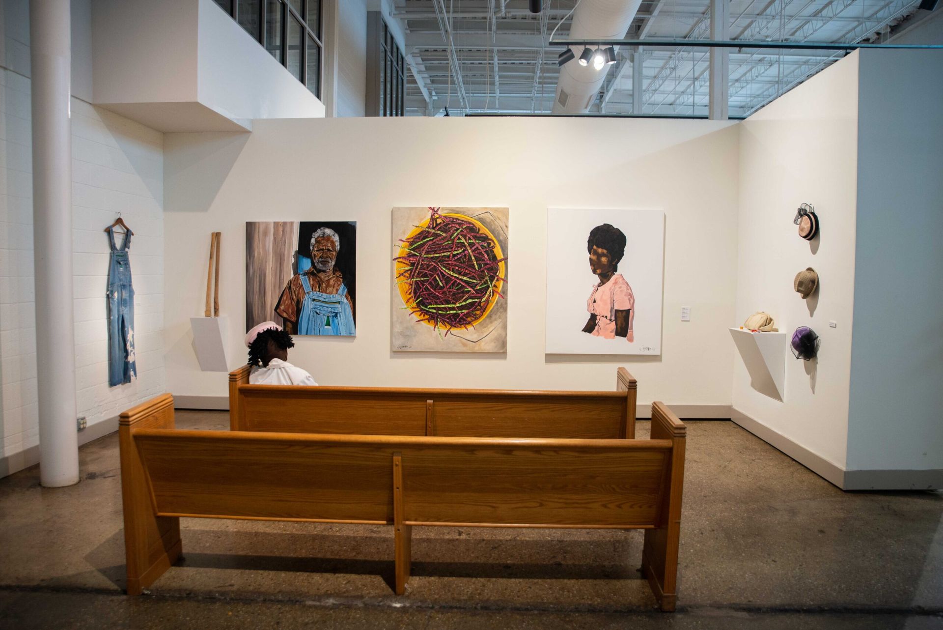 Art gallery interior with benches and framed portraits on white walls under a high ceiling.