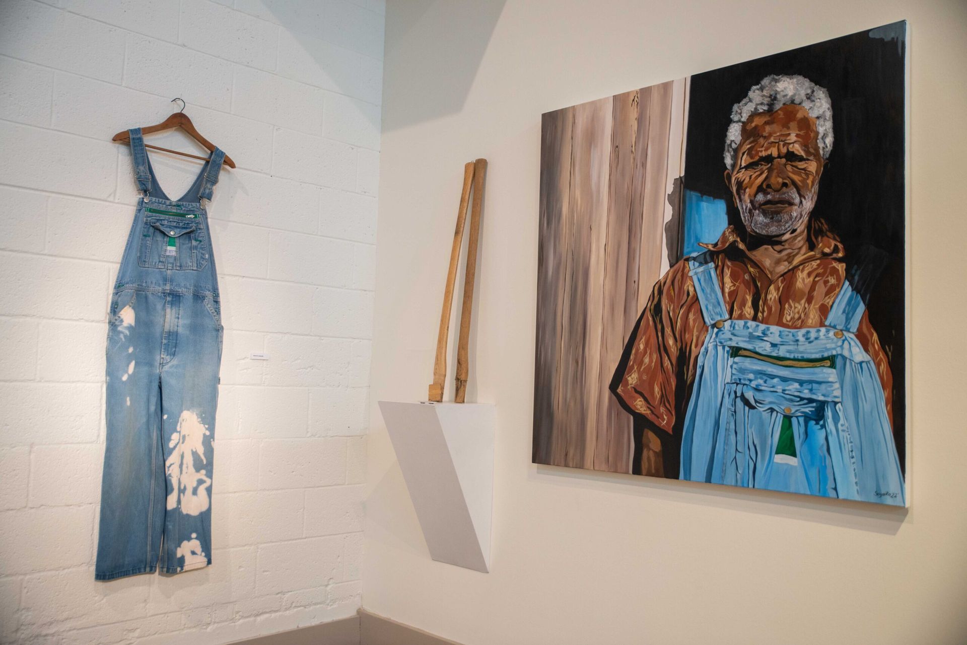 Gallery wall with a denim jumpsuit and a portrait painting of a person in overalls.