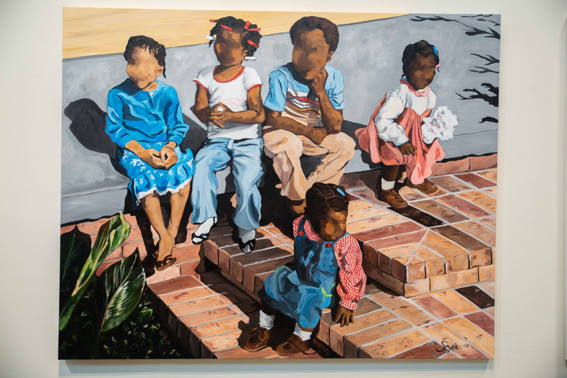 Children sitting on brick steps, one standing in front, wearing colorful clothes outdoors