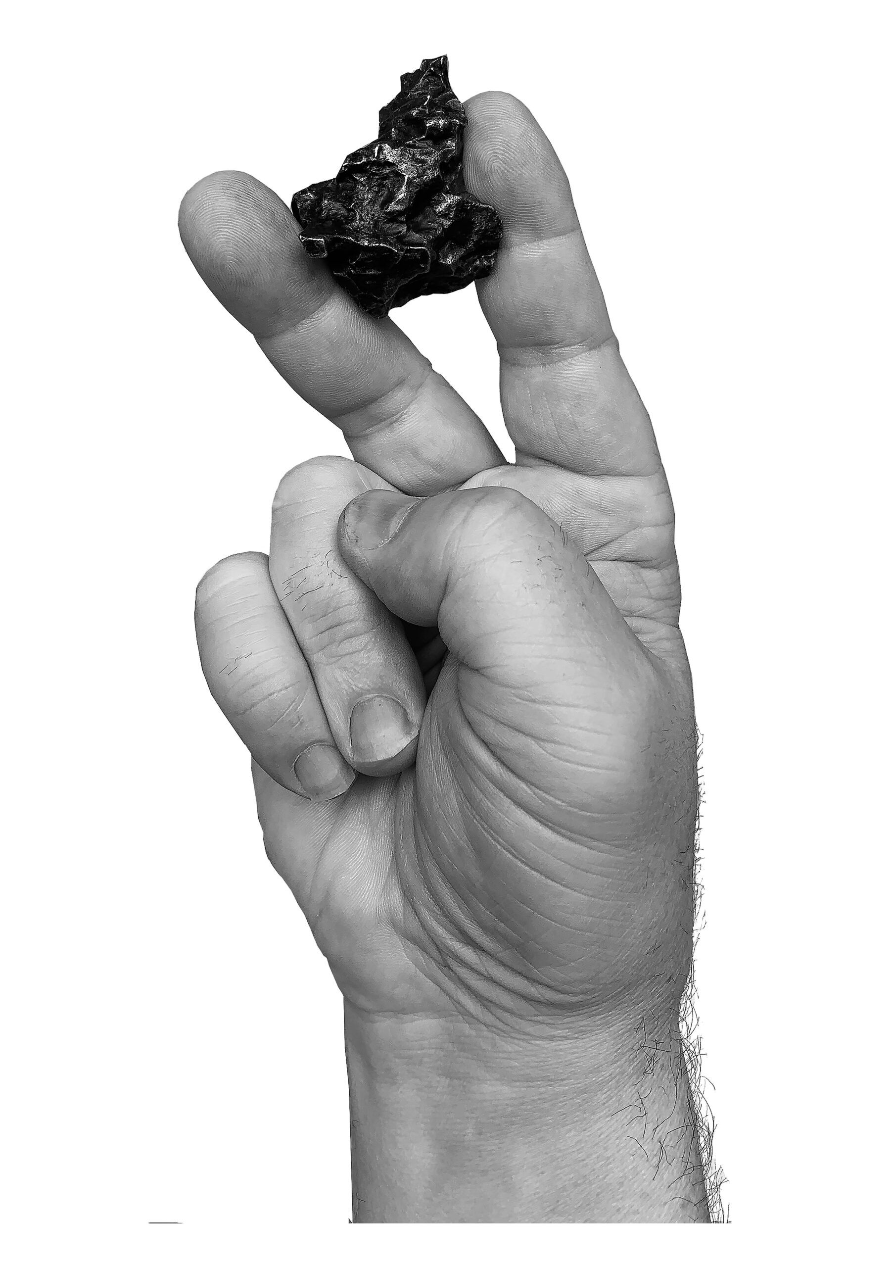 Hand making a pinching gesture while holding a small dark rock between two fingers.