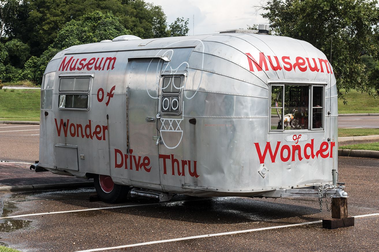 Small silver trailer labeled “Museum of Wonder” and “Drive Thru” in a parking lot