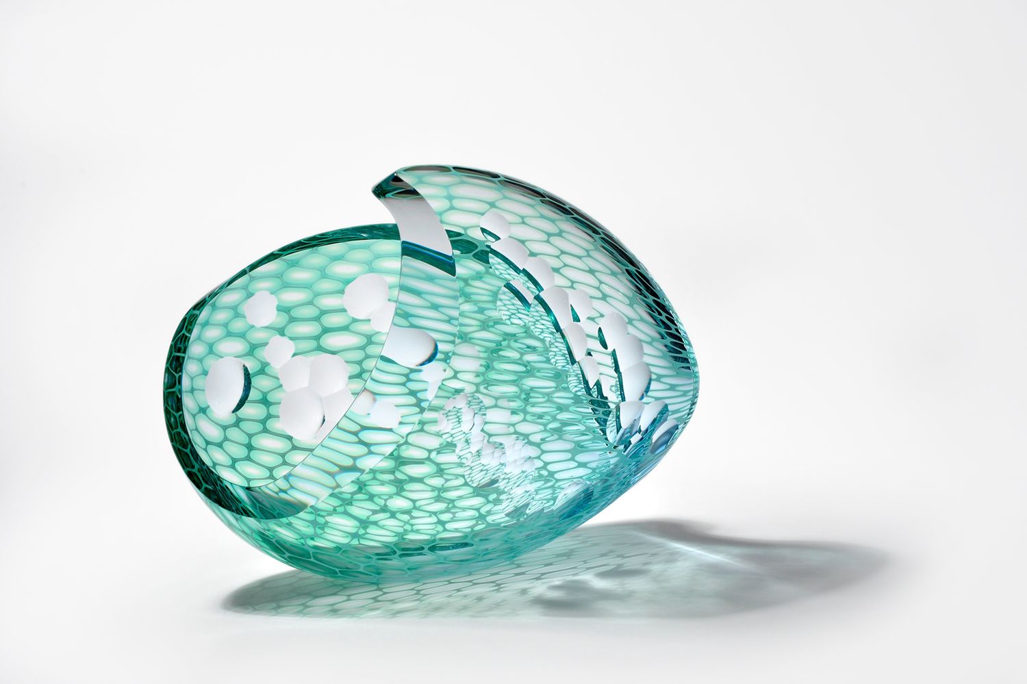 Translucent teal glass fish sculpture with white spots, resting on a white background