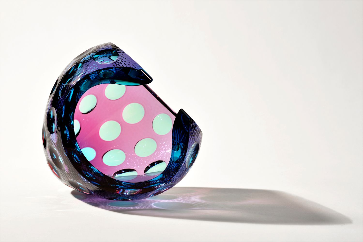 Abstract glossy crescent sculpture in black and pink with mint polka dots on a white background