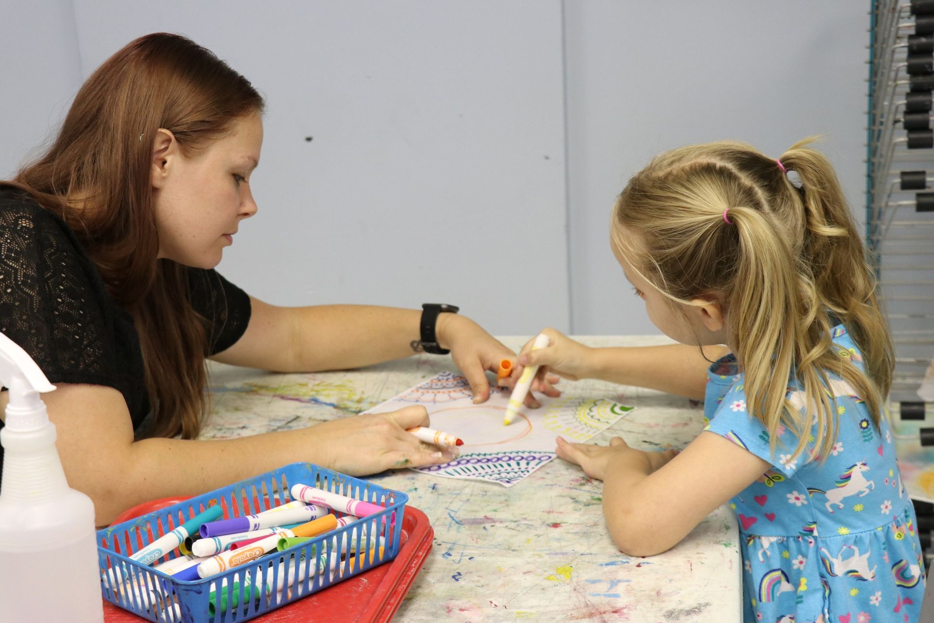 Two people drawing together at a table with crayons and art supplies