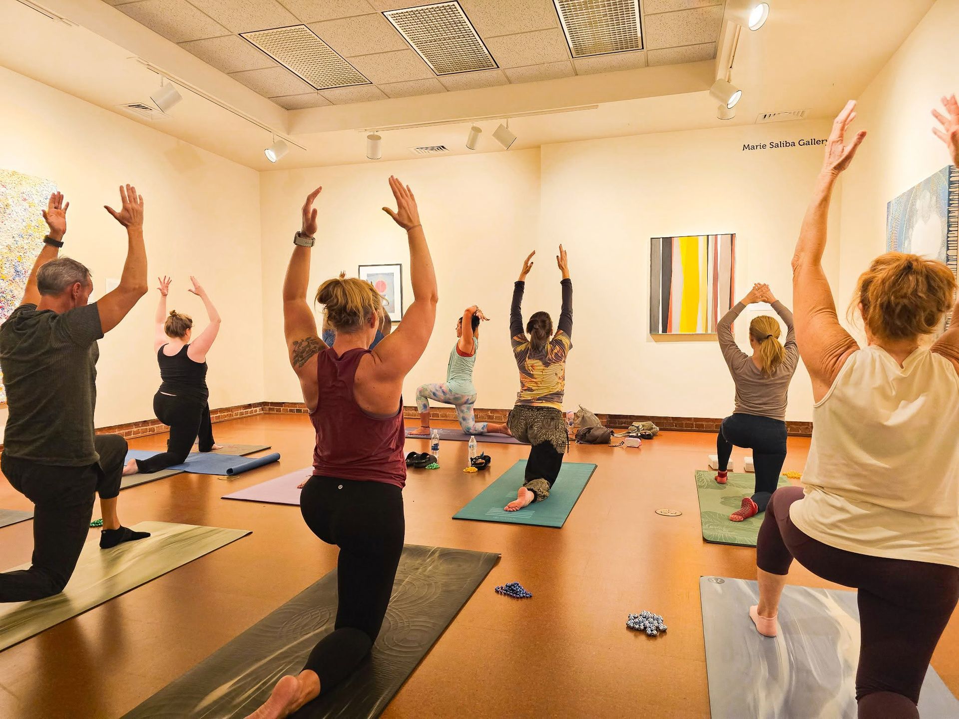 People doing yoga on mats in a bright studio, arms raised overhead.