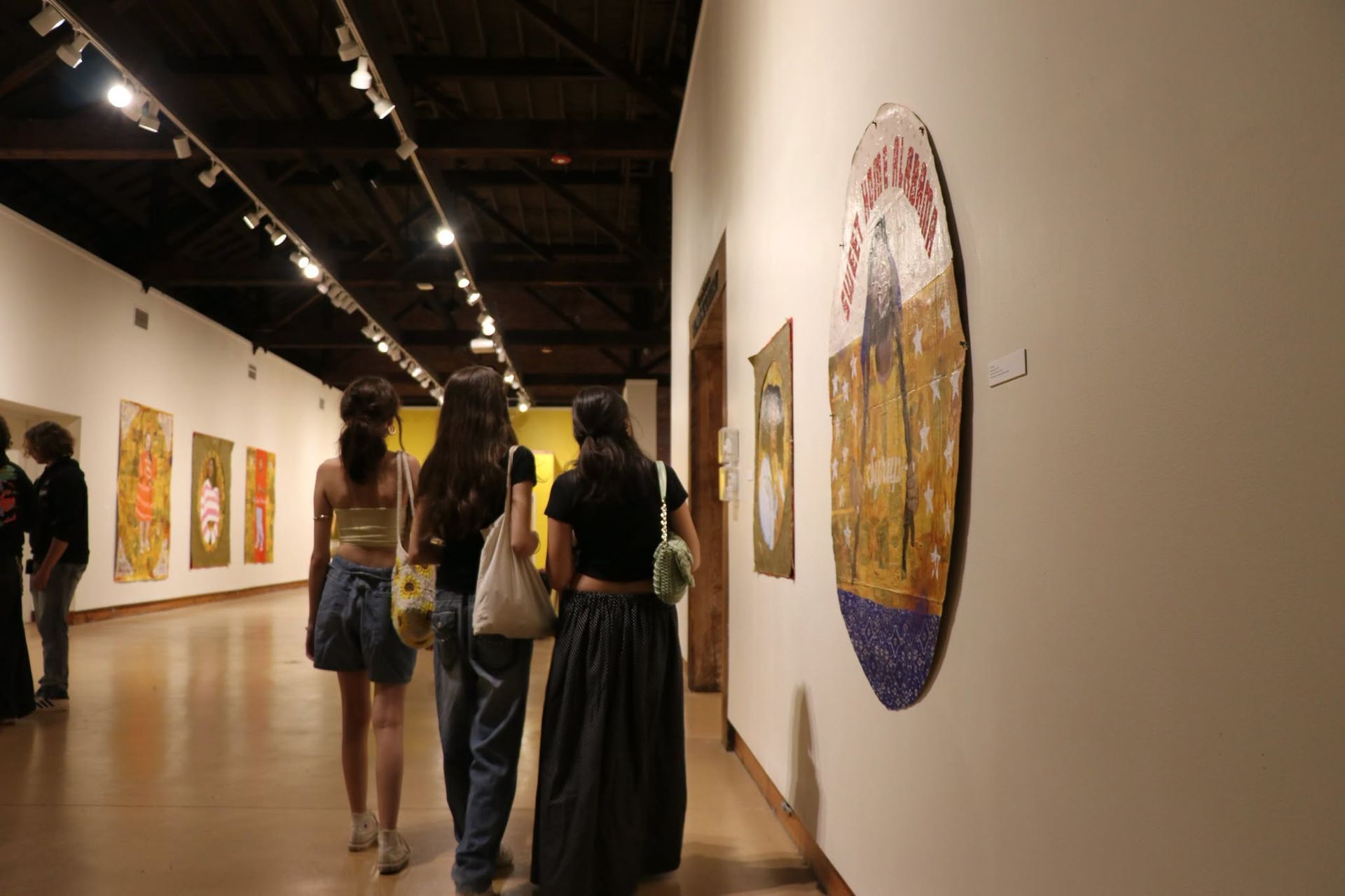 People viewing colorful paintings in a gallery with white walls and a polished floor
