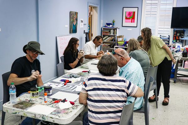 People seated at a craft table, painting and working in a bright art studio