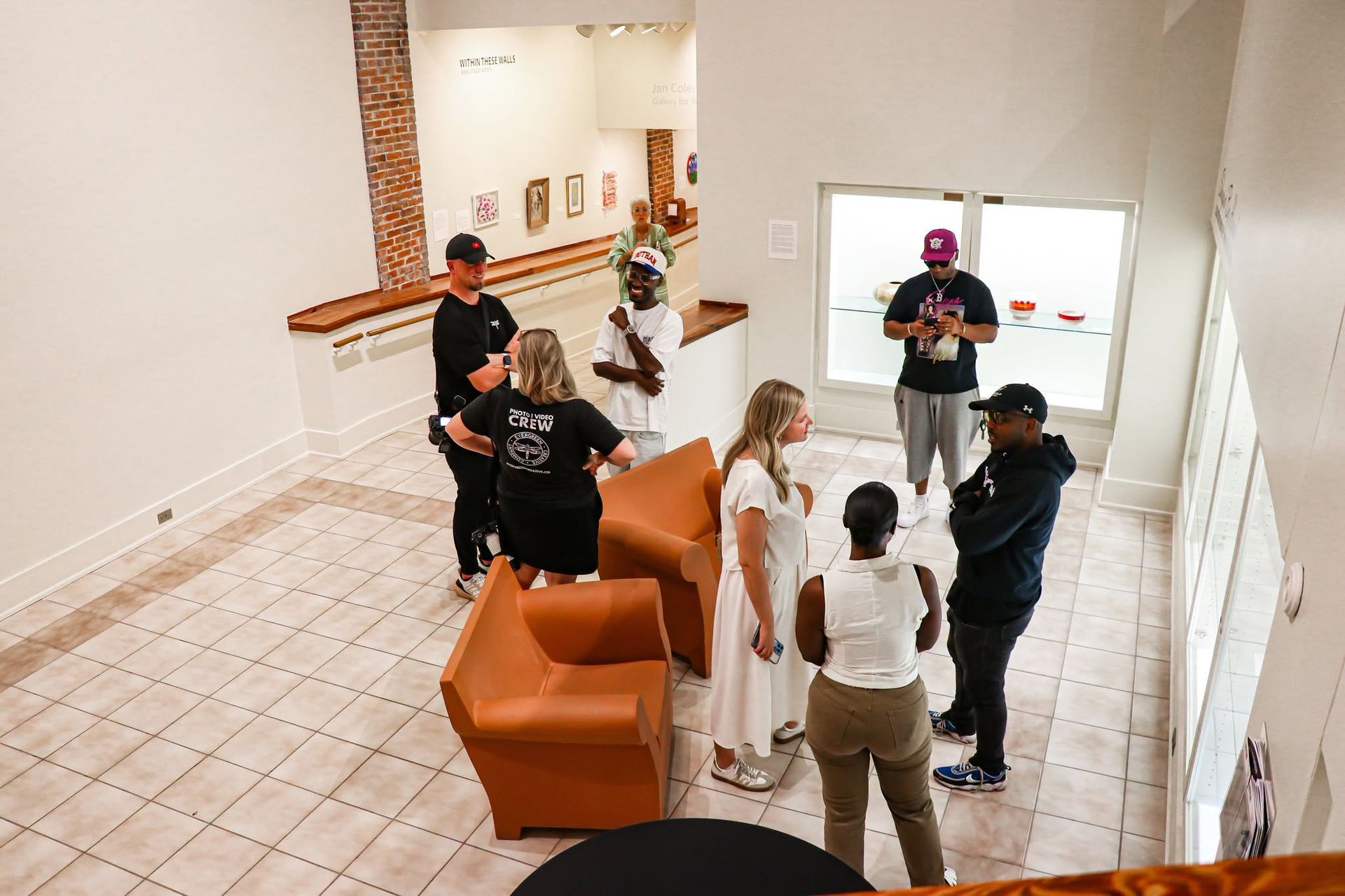 People gathered around orange chairs in a bright lobby, chatting and holding drinks.