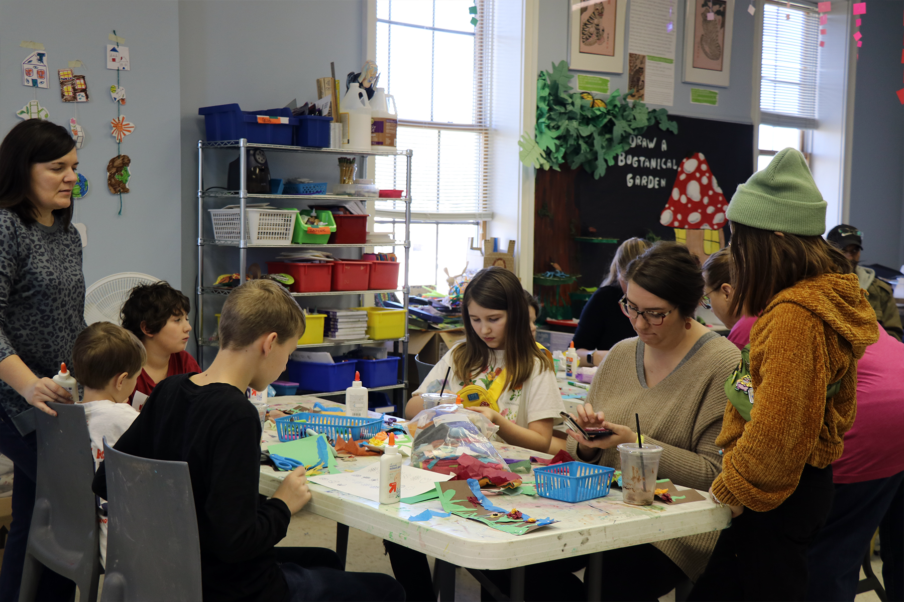 People gathered around a craft table in a bright classroom, making colorful art projects.