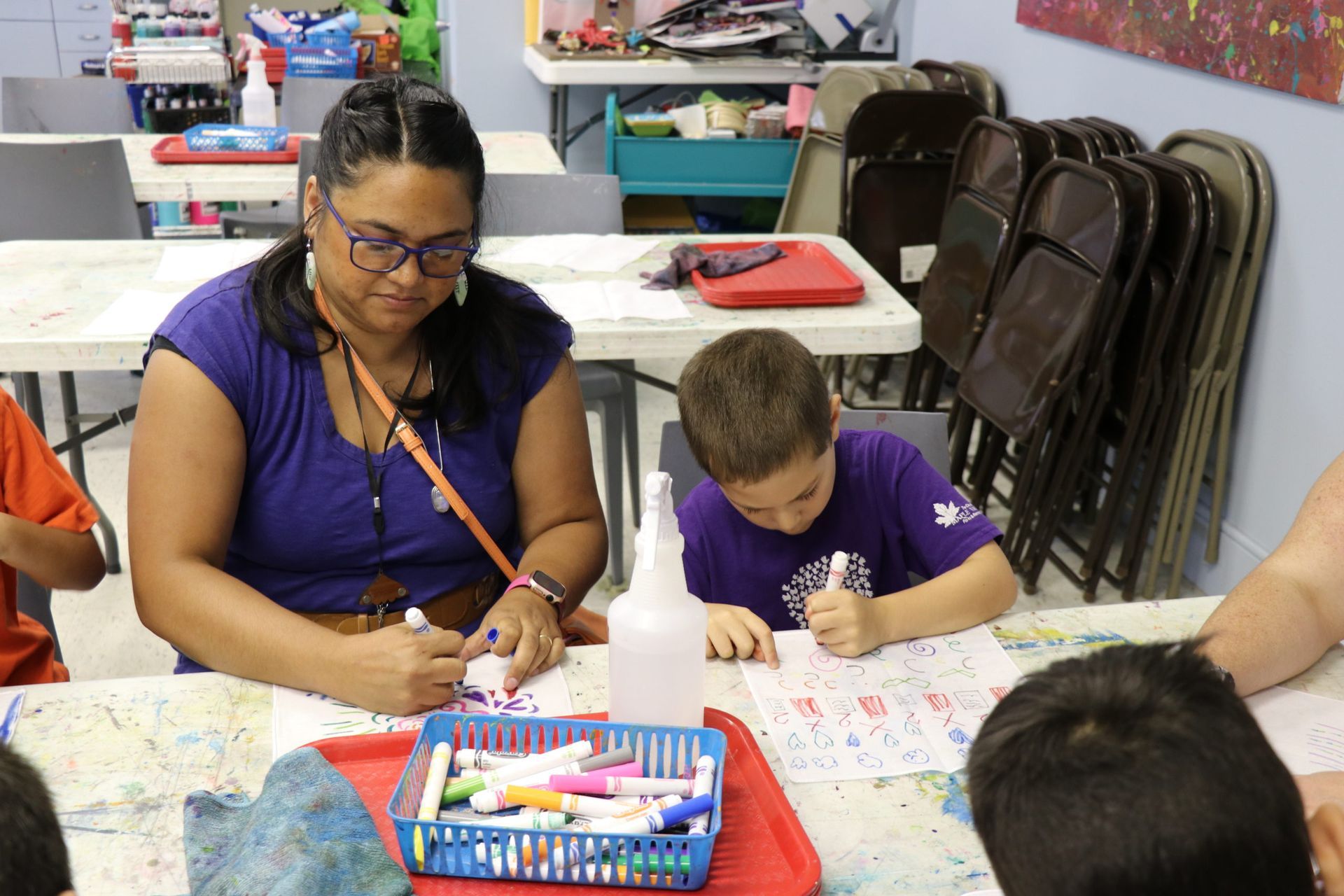 Woman and child coloring at a table with crayons in a classroom or art activity setting