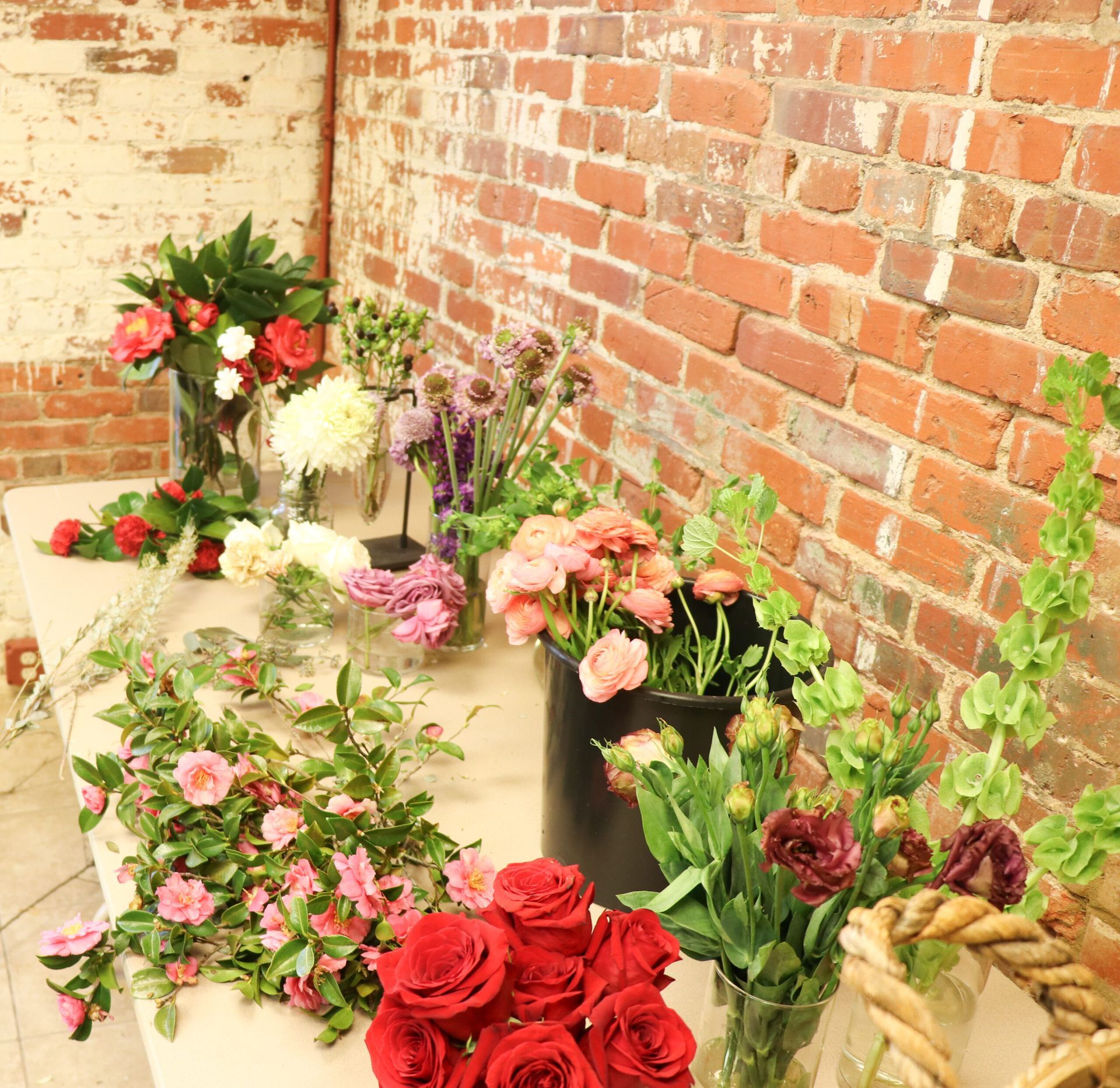 Assorted colorful flower bouquets arranged along a brick wall on a sunlit patio.