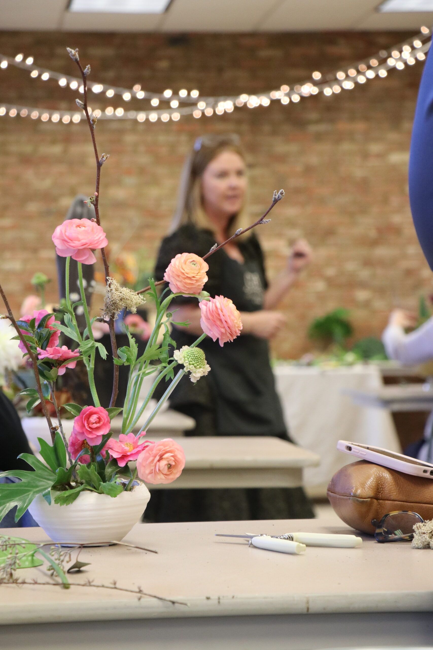 Flower arrangement on a table at an indoor event, with pink blooms and string lights in the background.