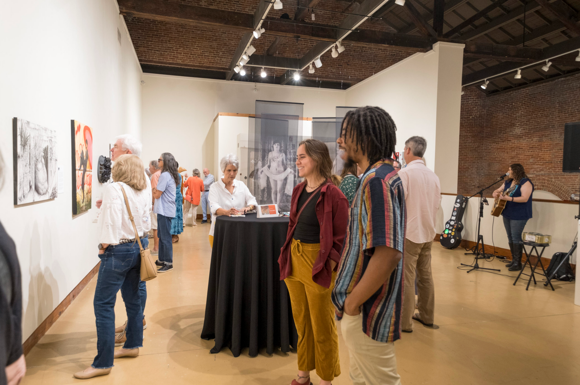 Art gallery reception with guests viewing paintings and mingling around a black cocktail table