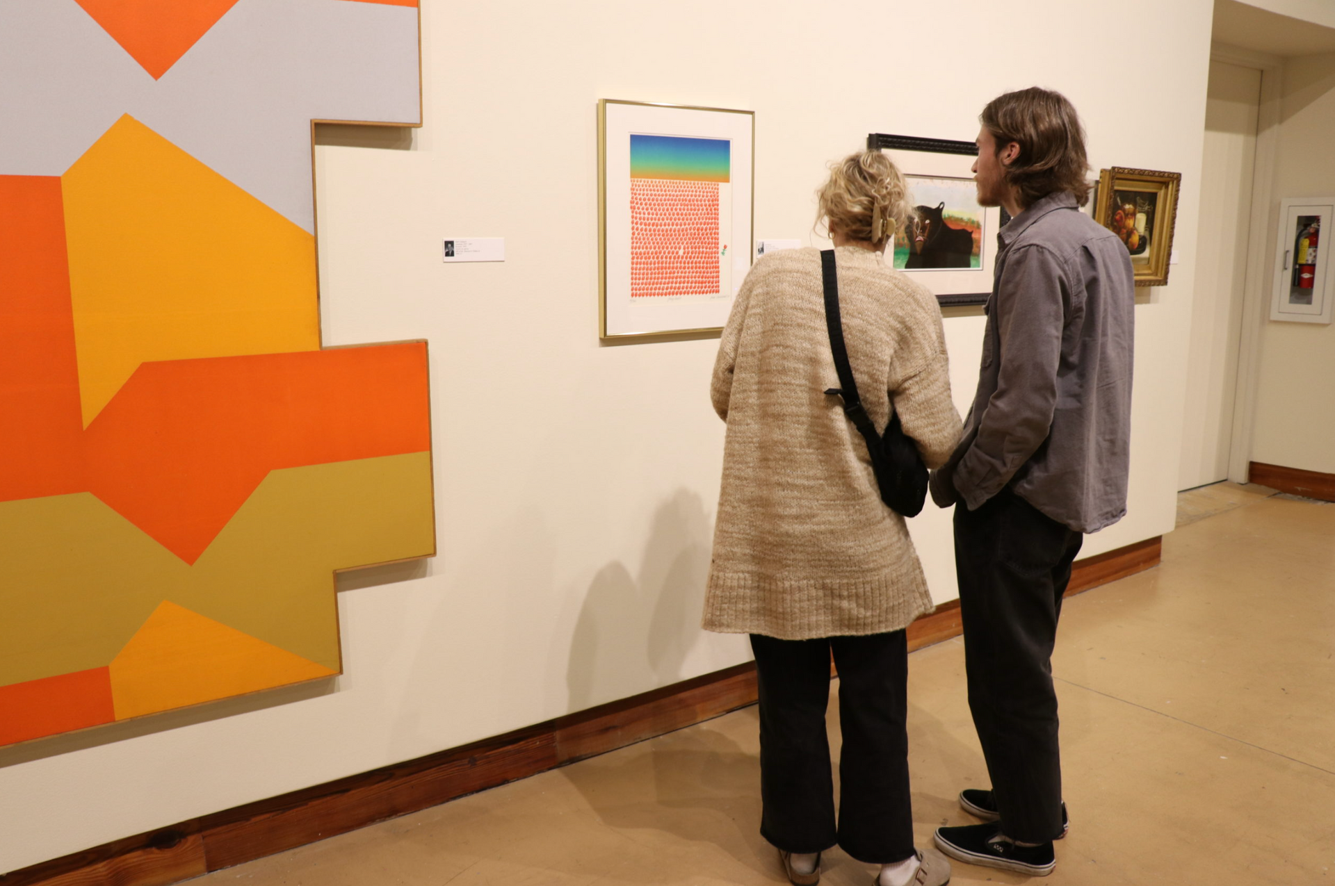 Two people viewing colorful abstract paintings in a gallery hallway