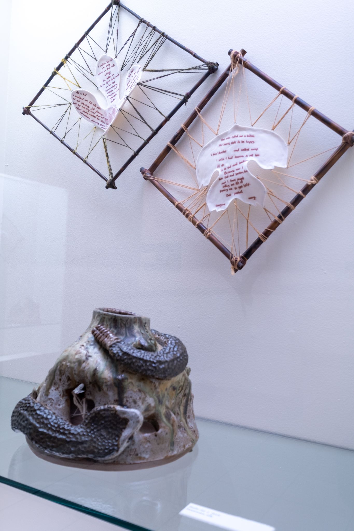 Abstract sculpture of two wire-framed square panels above a gray sculpted base on a glass shelf