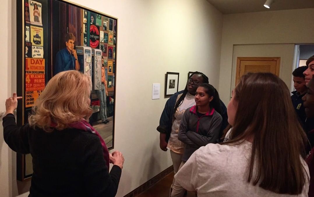 People viewing artwork in a gallery hallway, with colorful framed pieces on the wall.