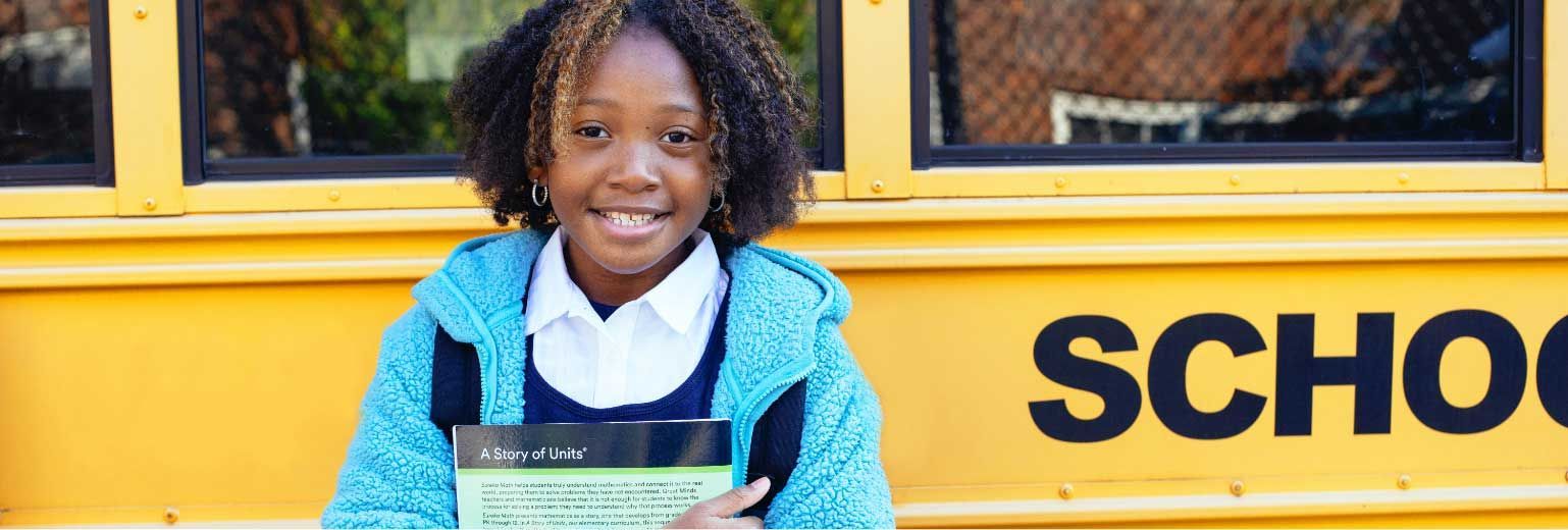 Smiling student in blue sweater holding a certificate in front of a yellow school bus