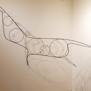 Abstract black line drawing of overlapping circles on a white wall, resembling a long animal or flowing form