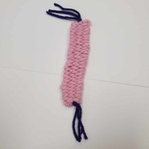 Pink knitted strip with dark blue yarn loops at the top and bottom on a white background
