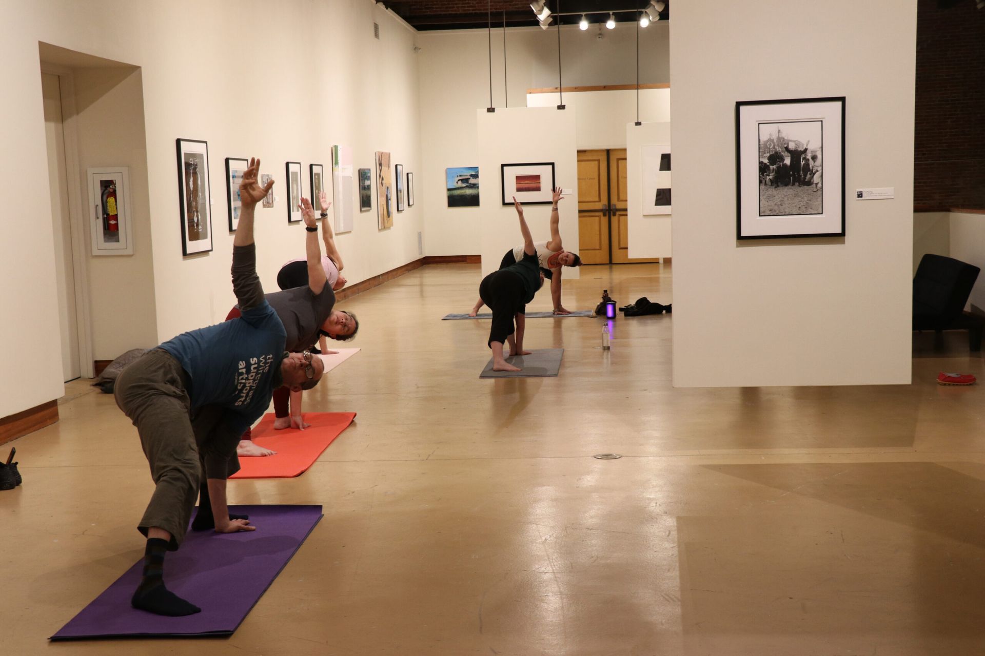 People doing yoga poses on mats in an art gallery with framed pictures on the walls