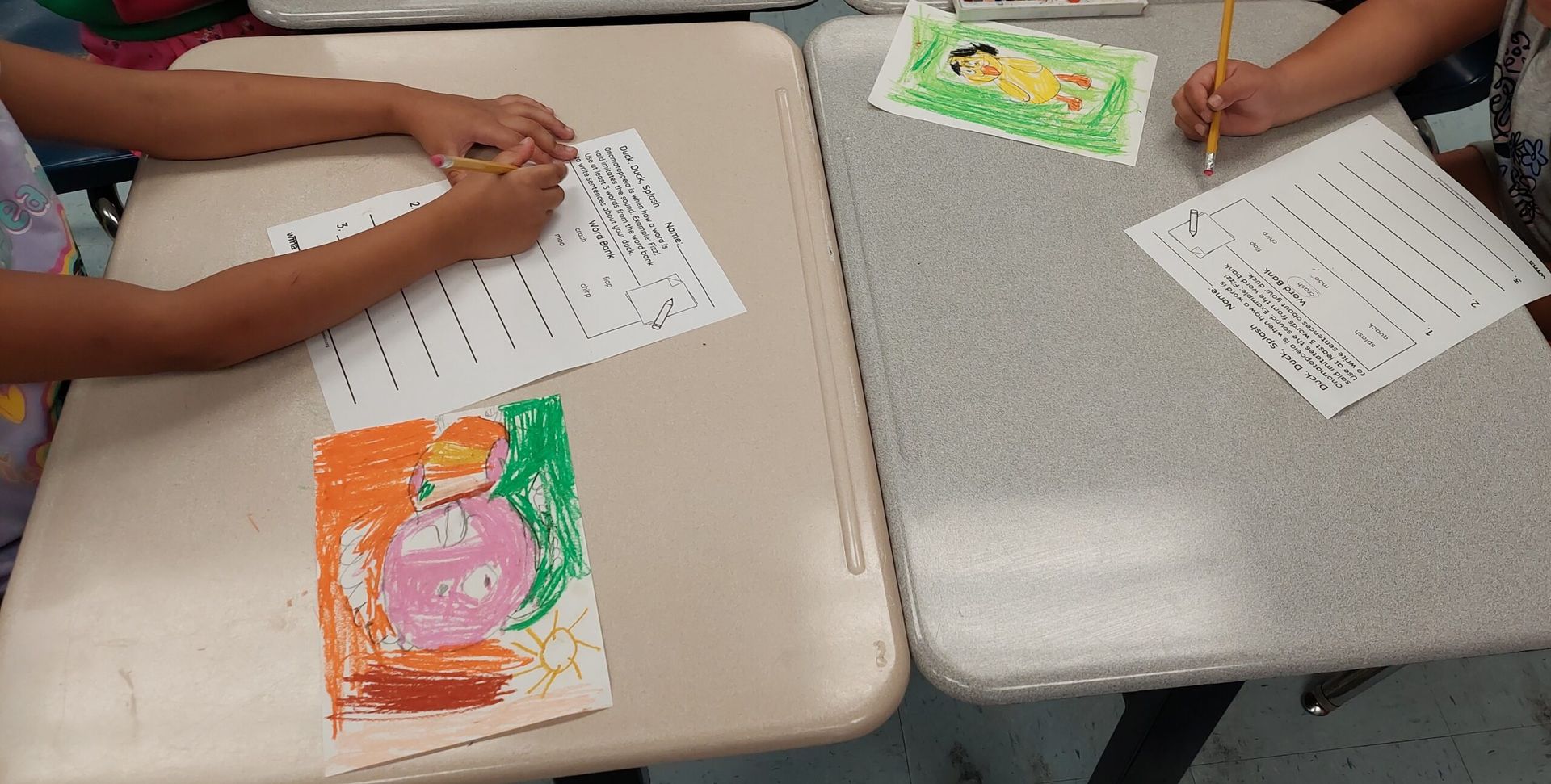 Children coloring worksheets at a classroom table, with bright orange, green, and pink artwork.