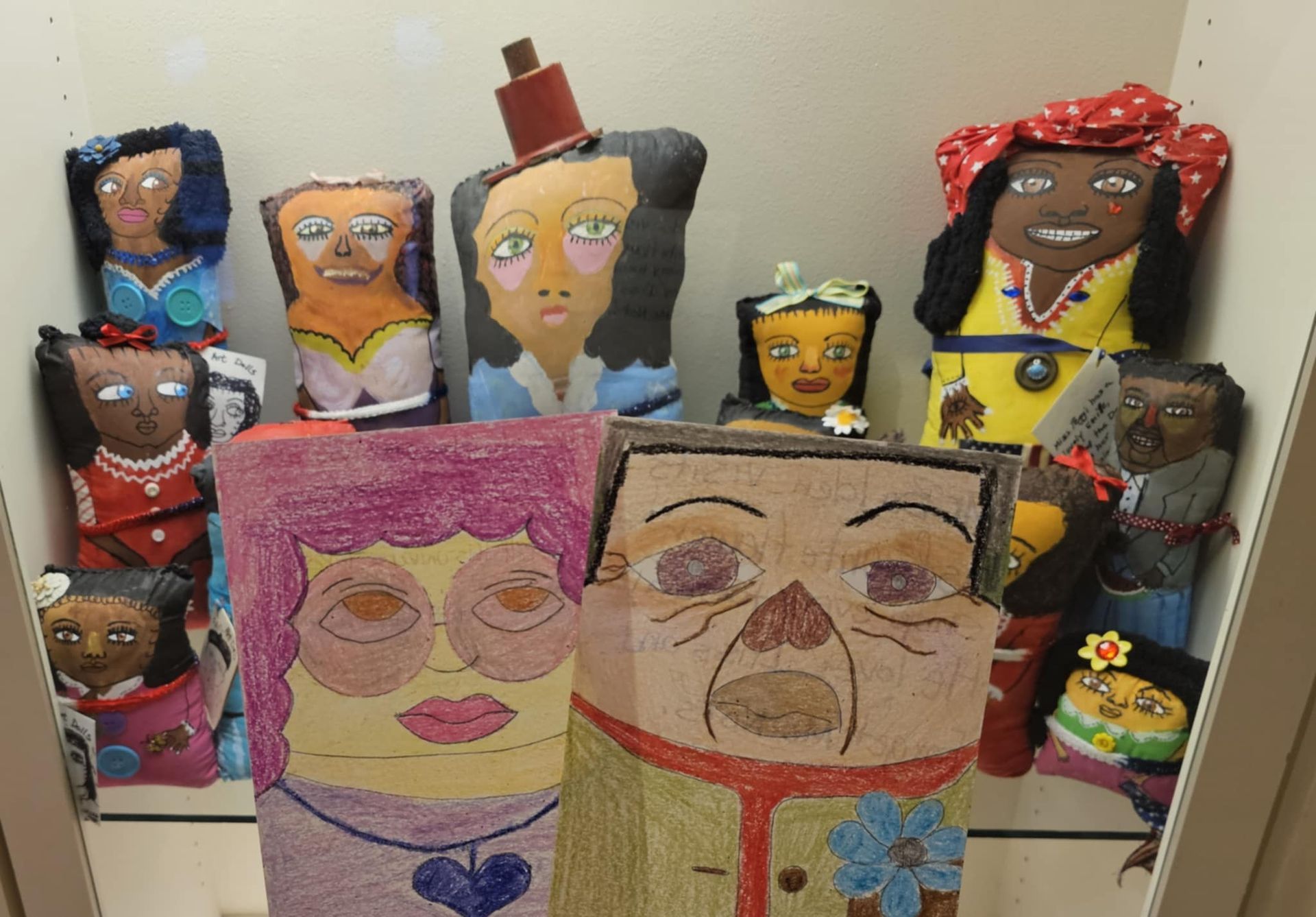Colorful handmade paper-mache faces arranged on shelves, with large smiling portraits in the front.