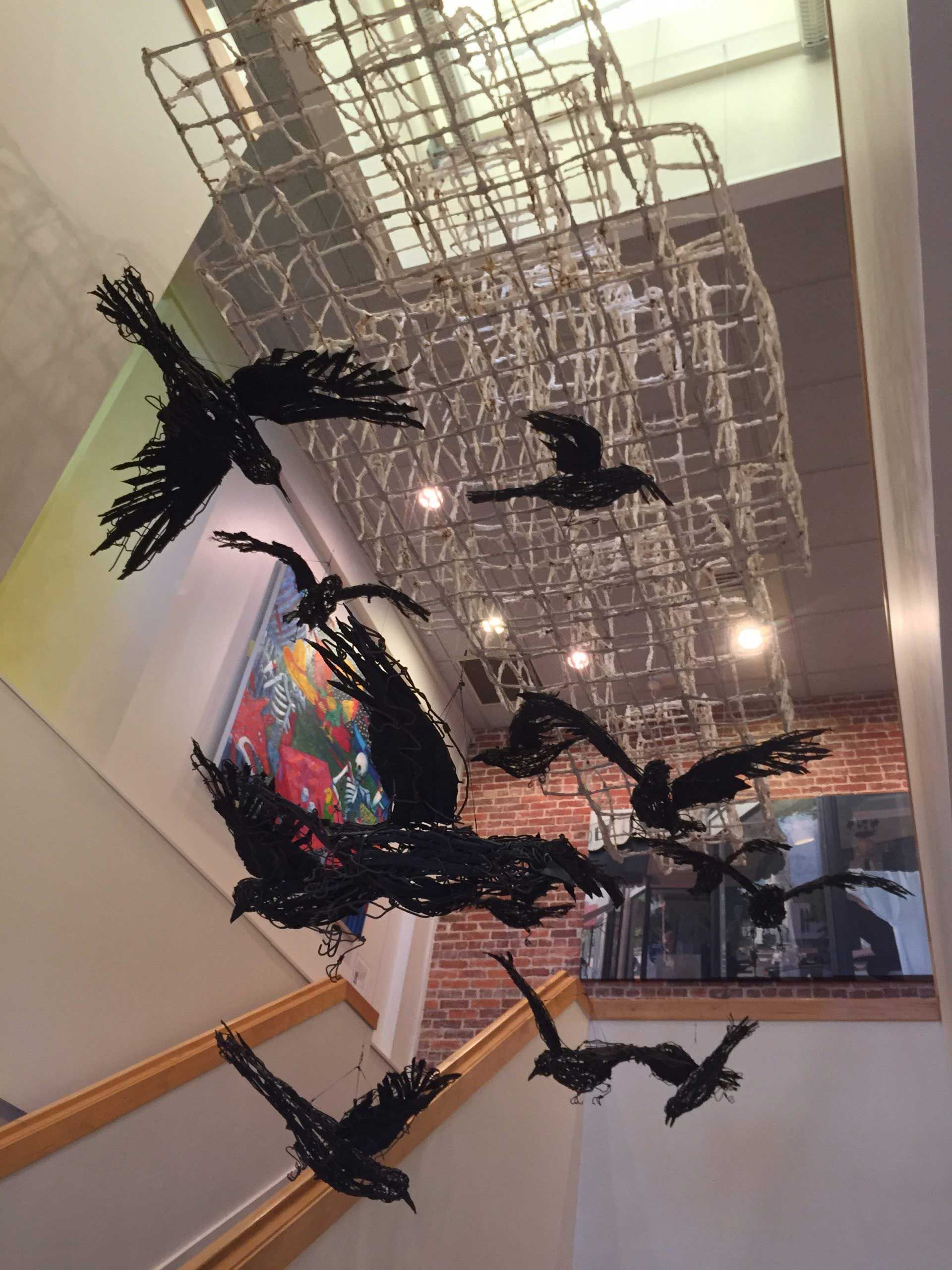 Abstract black hanging sculptures in a bright indoor gallery with a red-and-blue center piece.