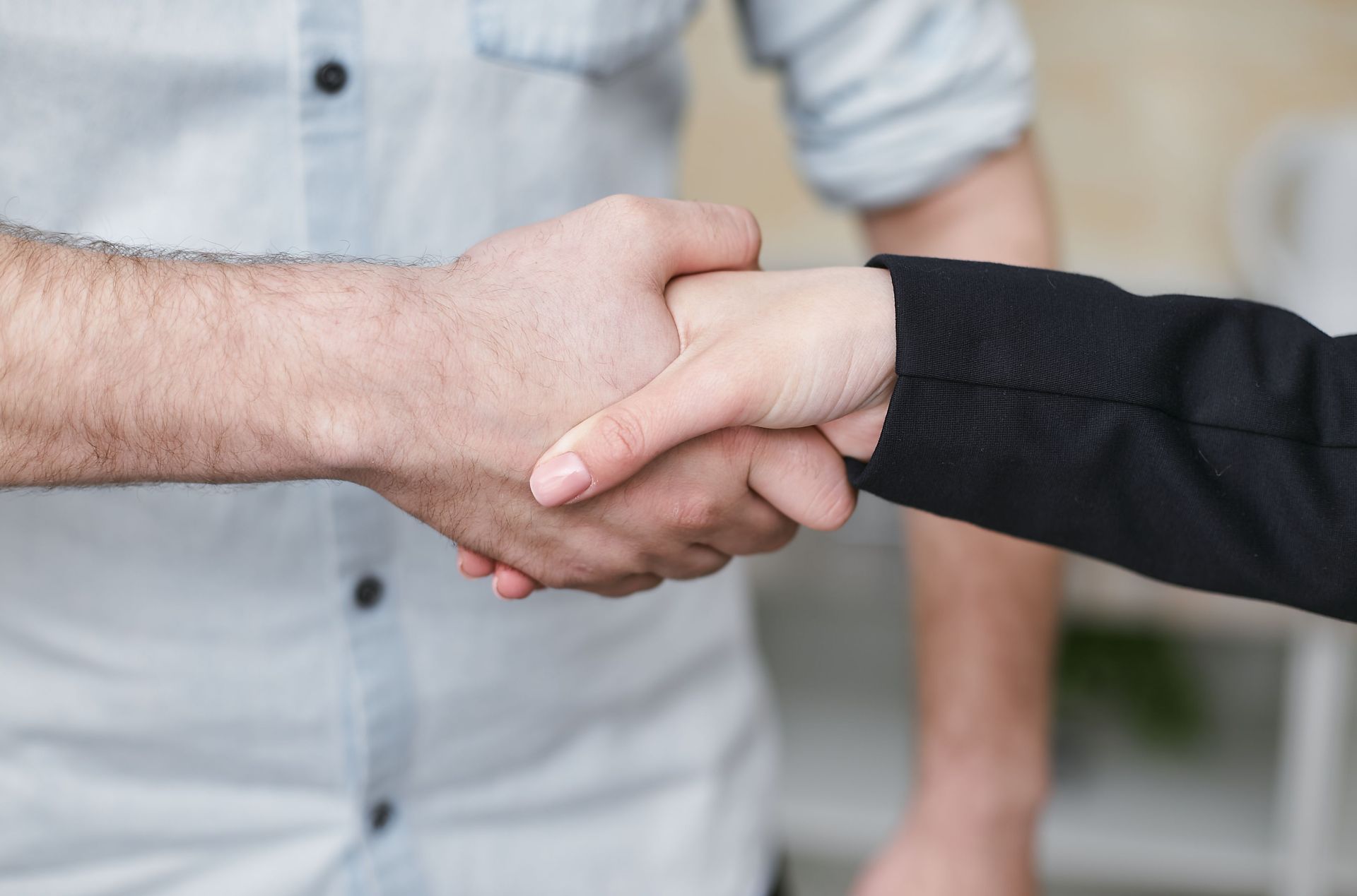 Two people shaking hands, one in a light shirt and one in a black sleeve, indoors.