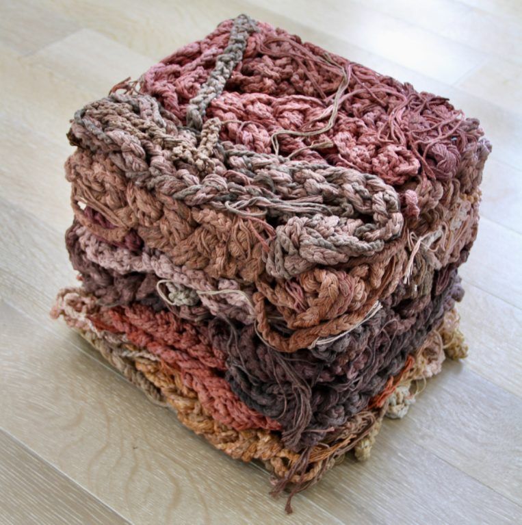 Stacked handmade crocheted fabric baskets in pink, brown, and beige tones on a wooden floor