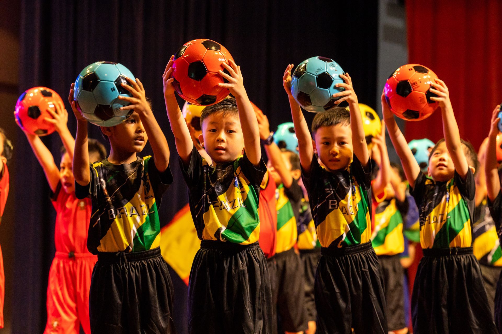 Children in matching shirts hold up soccer balls on stage.
