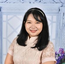 Woman with black hair smiling, wearing a pink lace top and pearl headband, against a floral background.