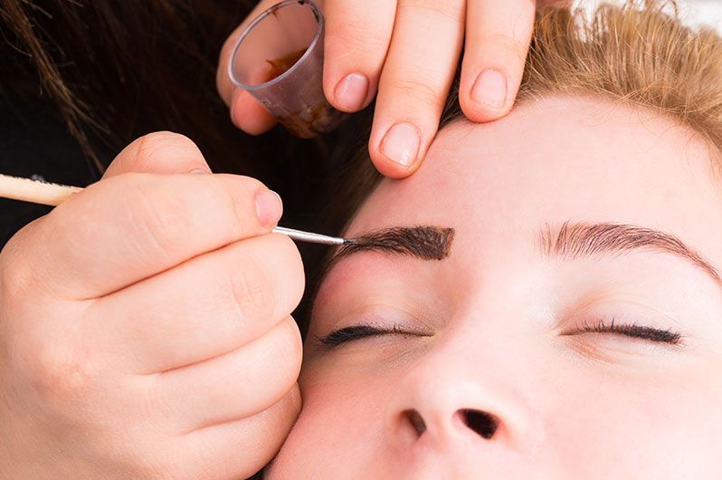 A woman is getting her eyebrows painted by a makeup artist.