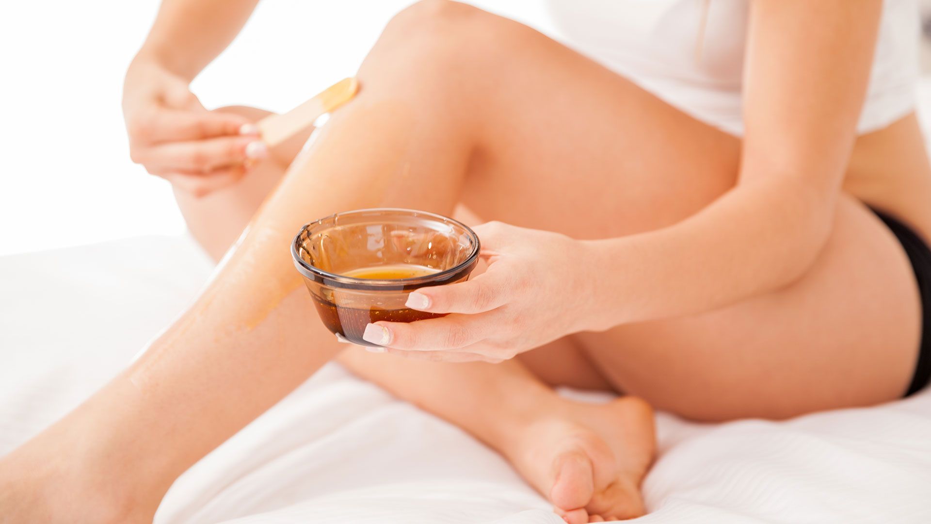 A woman is waxing her legs with a bowl of wax.