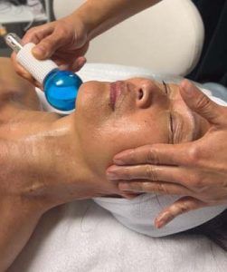A woman is getting an ice ball treatment on her face.