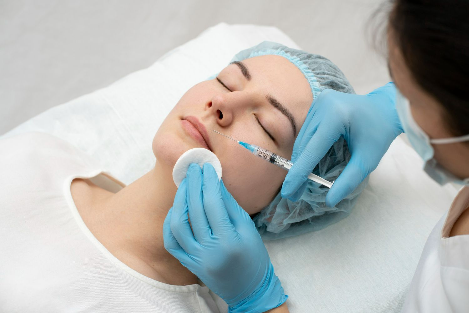 Woman receiving facial injection from a medical professional wearing gloves. White setting.