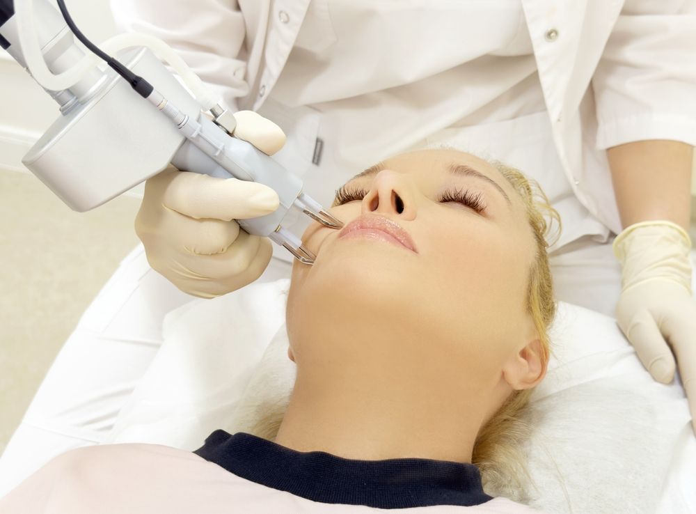 Woman receiving laser skin treatment on her face from a gloved medical professional in a clinical setting.