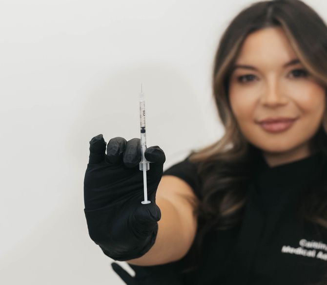 Gloved hand holding a syringe toward the camera, with a woman blurred in the background