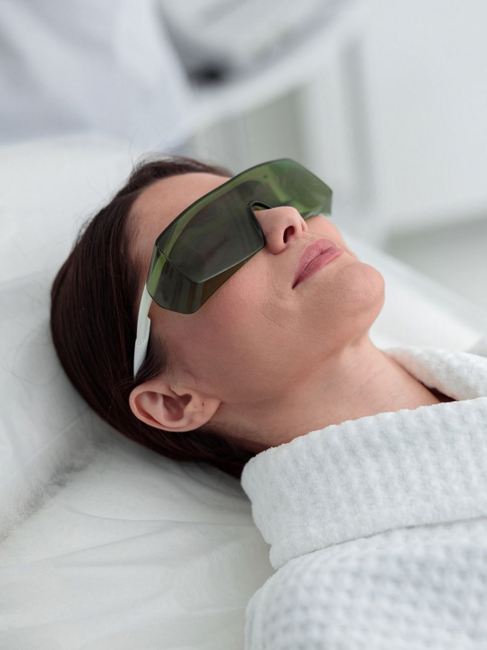 Woman wearing protective glasses, lying down, ready for a cosmetic procedure.