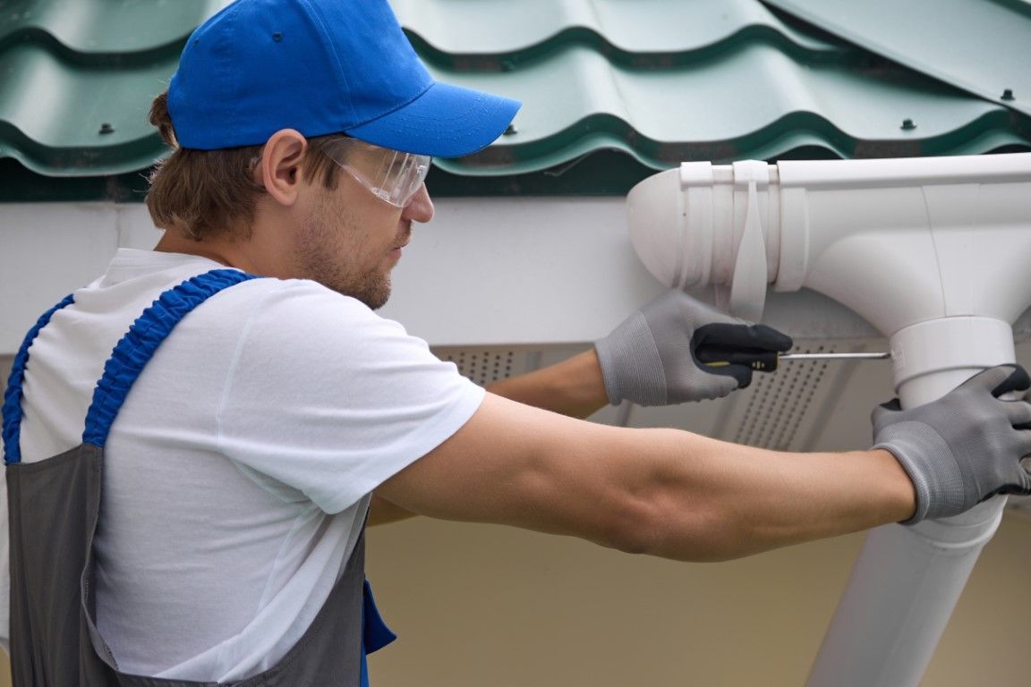 Gutter guard on a roof with a leaf blower nozzle cleaning debris along the edge