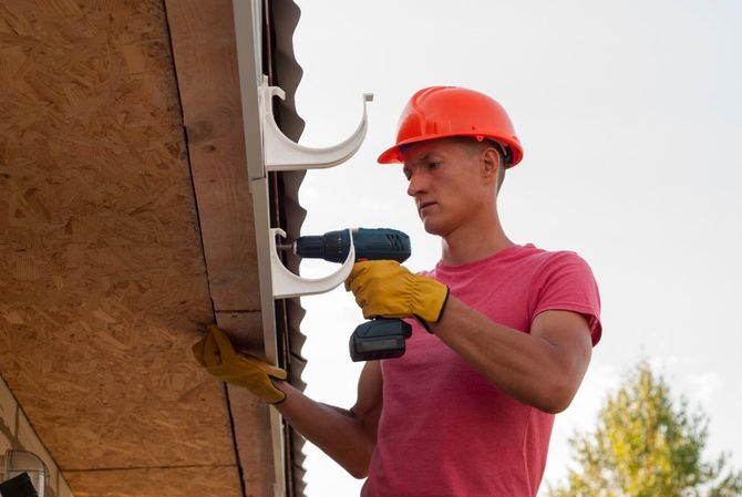 Worker in orange hard hat drilling under a roof eave outdoorsF