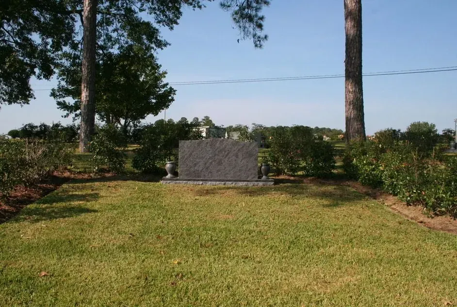 Memorial stone in a grassy park with trees and hedges under a clear blue sky