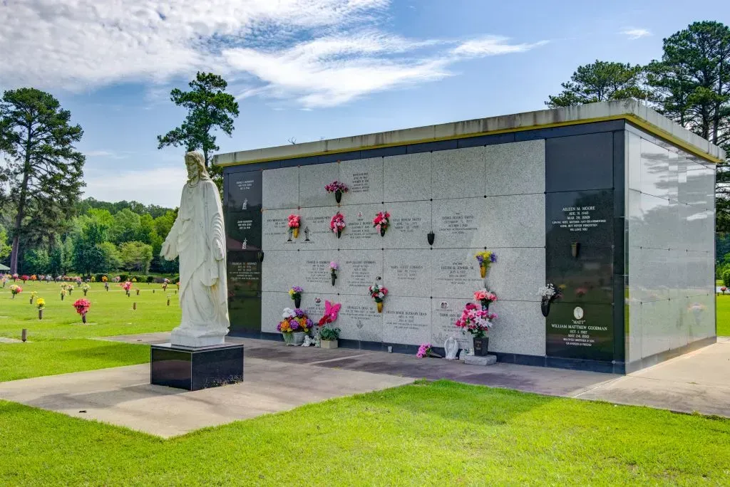 Outdoor mausoleum with flowers and a white statue in a green cemetery lawn