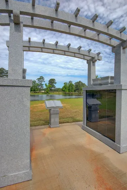 Outdoor pavilion with curved white beams, a kiosk, and grassy field beyond