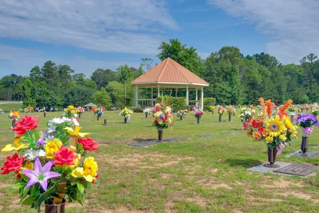Flower bouquets in a grassy park near a gazebo under a blue sky.
