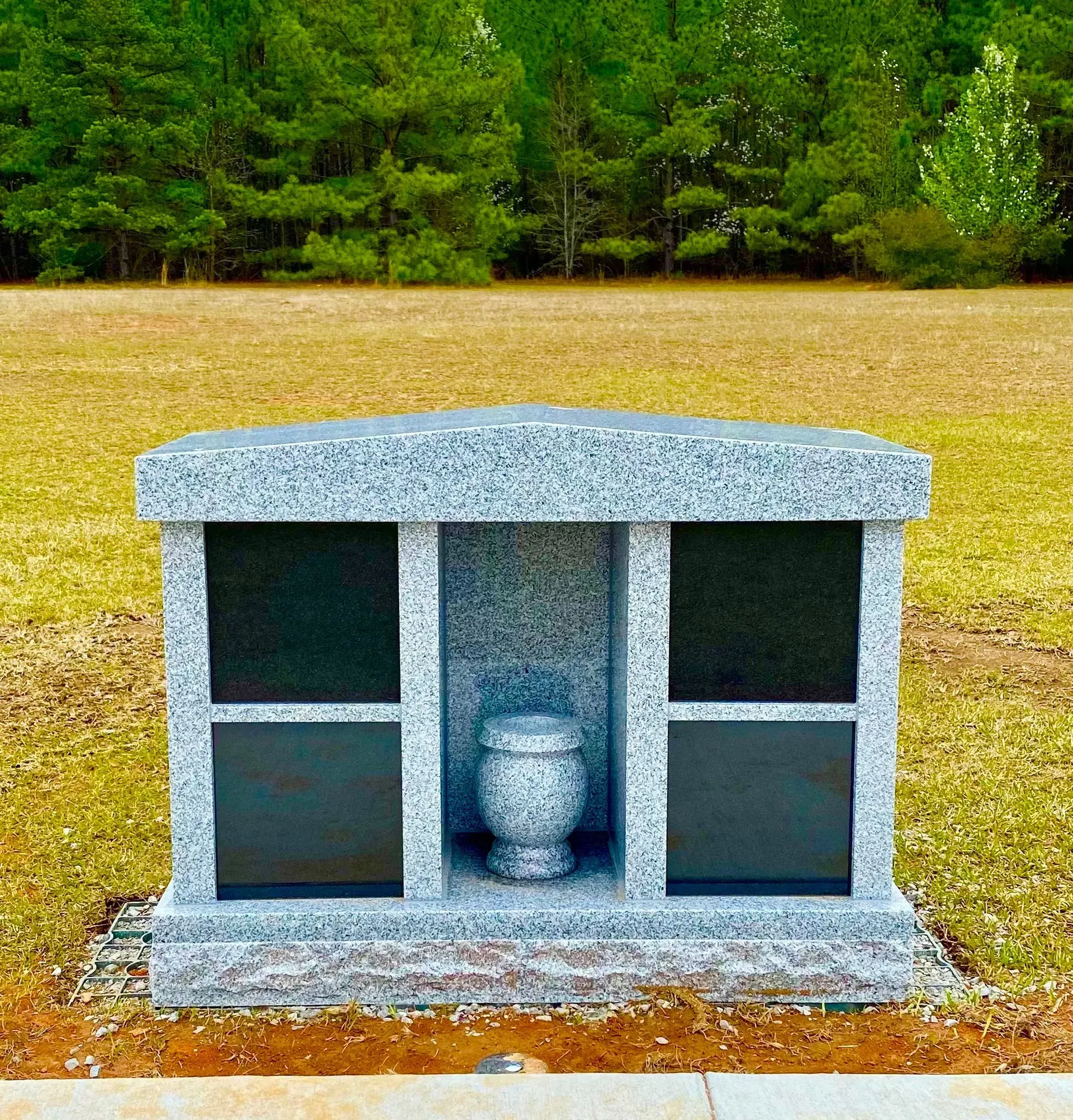 Granite memorial with a vase, centered on a grassy cemetery plot