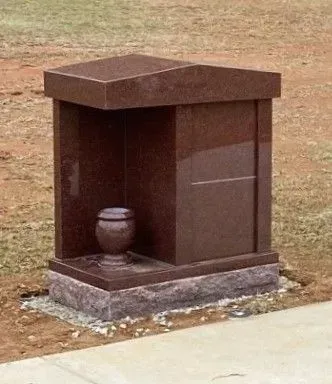 Small brown outdoor urn niche monument on a concrete base beside a walkway.