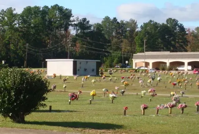 Grassy field with many colorful memorial markers, trees in back, and a white pavilion under a blue sky