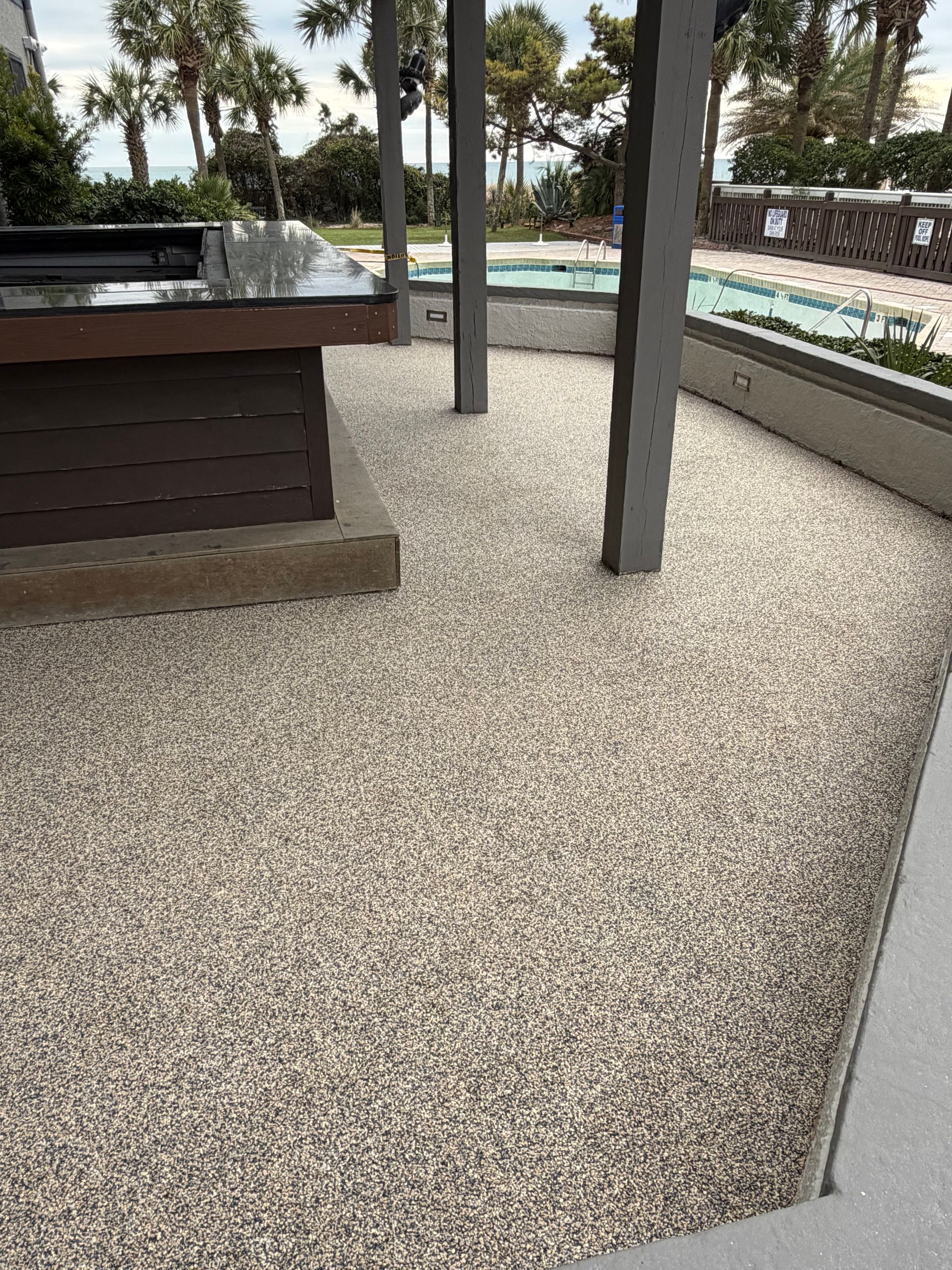 Outdoor patio with gravel flooring, dark posts, and a pool area in the background
