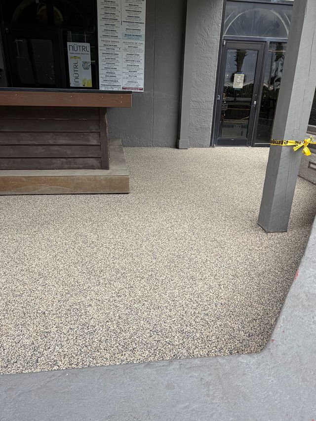 Storefront entrance with speckled sidewalk, gray pillar, and yellow caution tape near the doorway